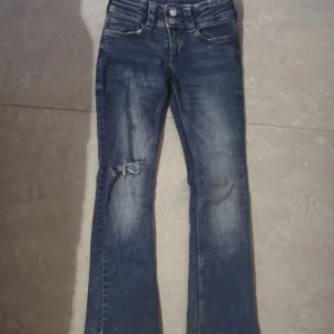 Blå lowaist bootcut jeans från H&M, stl 140 - Snygga blå bootcut jeans från H&M med låg midja och justerbar midja. Jeansen har slitning och hål på ena benet som jag har gjort själv.  Materialet är bomull med lite stretch. Ett av mina gamla favoritbyxor men för små❤️