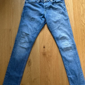 Ljusblå jeans från Jack & Jones 31/34 - Säljer ett par ljusblå jeans från Jack & Jones i modellen Jeans Intelligence. Jeansen har slitna detaljer på låren och knäna, klassisk femficksdesign och raka ben. Tillverkade i bomull med en skön passform som funkar till det mesta.