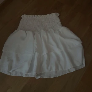 Vit volangkjol med smock - Supersöt vit kortkjol med smock i midjan och dubbla volanger. Endast provad 