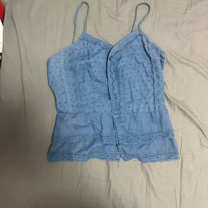 Blå spetsdetaljerad linnetopp Fornarina - Supersöt blå linnetopp från Fornarina med tunna axelband, knappar framtill och spetsdetaljer längs kanterna. Prickigt mönster upptill och broderade band nertill ger en romantisk vibe. Perfekt för varma dagar och sommarhäng! Står storlek L men passar mer s/m, helt ny med prislapp