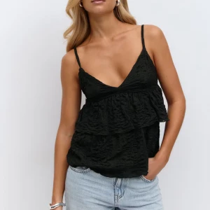 Svart volangig linnetopp med smala band - Supersnygg svart linnetopp med smala axelband och djup v-ringning. Toppen har dubbla volanger och en lätt skrynklig struktur som ger en cool och trendig look. Perfekt att matcha med jeans eller kjol för en chill stil. Nypris:299