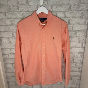 Ralph Lauren skjorta - Snygg korallrosa skjorta från Ralph Lauren i mycket fint skick, endast en liten markering vid vänster ärmslut, syns knappt vid användning (se bild). Skön passform och stilren look – perfekt till både vardag & fest! Hör av dig vid intresse! 🙌