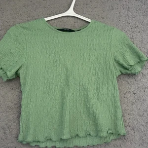 Grön t-shirt - Superfin ljusgrön croppad topp från Vero Moda med korta ärmar och vågig kant nertill. Perfekt till jeans eller kjol för en fräsch look. Endast använd ett fåtal gånger✨💕.