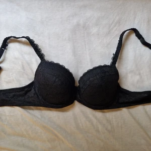 Oanvänd bh - Snygg svart pushup bh från Serenity i storlek 75B. Bh:n har vadderade kupor och är täckt av fin spets med dekorativ kant upptill. Axelbanden är justerbara och materialet är mjukt och bekvämt. Perfekt för dig som gillar en klassisk och stilren look.