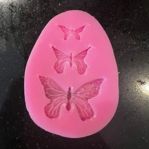 Silikonform - fjärilar  - Bilderna visar en rosa silikonform med tre fjärilsmotiv i olika storlekar. Formen är perfekt för att skapa dekorationer till bakning, pyssel eller DIY-projekt. Passar dig som gillar att vara kreativ och vill göra egna detaljer med fjärilstema. Pennan är till för att få en uppfattning om hur stor formen är. 
