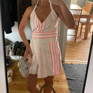 Randig omlottklänning i pastell - Superfin kort omlottklänning med halterneck och v-ringning. Klänningen har pastellfärgade ränder i rosa, vitt, gult och ljusblått samt dekorativa knappar i midjan.  Skulle säga att den är liten i storlek perfekt för M/S