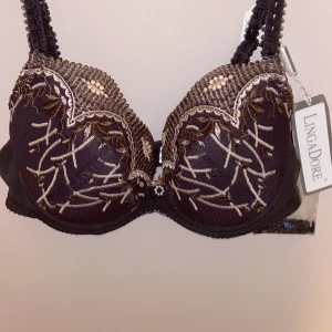 Brun push-up bh från LingaDore helt ny - Nypris 440kr           Snygg brun push-up bh från LingaDore med broderade detaljer i beige och guld. Bh:n har vackert blommönster, spetskant och en liten glittrig dekoration mellan kuporna. Axelbanden är dekorerade och det följer med extra tillbehör.