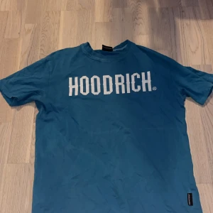 Blå HOODRICH t-shirt XS - Snygg blå t-shirt från HOODRICH i storlek XS. T-shirten har klassisk passform, korta ärmar och stort vitt tryck med HOODRICH-loggan på bröstet. Perfekt för dig som gillar streetwear och vill sticka ut med en enkel men stilren look. Den passar även Storlek S oxå en favorit men passar tyvärr inte längre