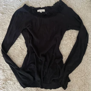 Svart topp med spets från Bik Bok - Svart långärmad topp från Bik Bok med snygg spetskant runt halsringningen. Modellen är tight och har en feminin, lite croppad passform. Perfekt att styla med jeans eller kjol för en trendig look.