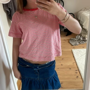 Randig rödvit t-shirt från Object - Säljer en kortärmad t-shirt från Object i storlek S. T-shirten är vit med tunna röda ränder och har en röd ribbad krage. Modellen är lite croppad och har en avslappnad passform. 