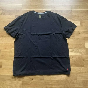 Ralph Lauren piké - Svart t-shirt från Polo Ralph Lauren i storlek XL. Klassisk modell med rund halsringning och korta ärmar. Tillverkad i mjuk bomull och har den ikoniska röda Polo-loggan broderad nertill. Perfekt basic-plagg med relaxed fit. Tröjan är i använt skick och kan ha lätt bleknad på färgen 