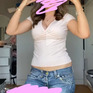 Ljusrosa v-ringad topp från Nelly - Supersöt ljusrosa topp med v-ringning och korta ärmar. Sitter figurnära och har en lätt rynkad detalj vid bysten som ger en snygg form. Perfekt att styla med jeans eller kjol för en fräsch look.