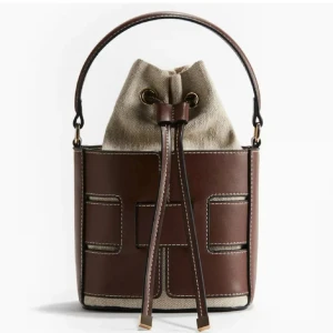 Brun bucket bag från hm - Snygg bucket bag i brunt skinn och beige canvas med coola kontrastsömmar. Väskan har ett stadigt handtag och stängs med snörning upptill. Perfekt för dig som vill ha en unik och trendig accessoar till vardagslooken. helt ny🩷