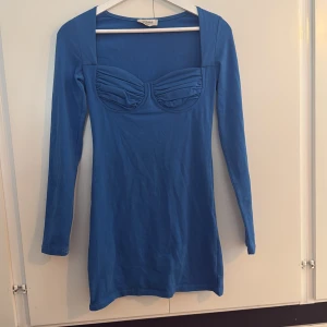 Blå långärmad kortklänning Chiquelle - Snygg blå kortklänning från Chiquelle med lång ärm och markerad byst med rynkade detaljer. Klänningen har en tight passform och fyrkantig ringning, perfekt för dig som vill sticka ut lite extra.