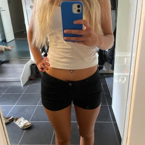 Svarta lågmidjade shorts - Säljer ett par svarta, tighta shorts med låg midja och klassisk jeanslook. De har fickor både fram och bak samt stängs med knapp och dragkedja. Perfekta för varma sommardagar och passar till det mesta. Snygg och enkel stil som är lätt att matcha. Har klippt av de så att de skulle bli kortare, därav priset!