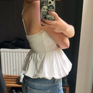 Vit volangig linnetopp med smala axelband - Supersöt vit topp med volangig, puffig nederdel. Toppen har en figurnära passform upptill och en luftig, flowy känsla nedtill. Inga defekter ❣️