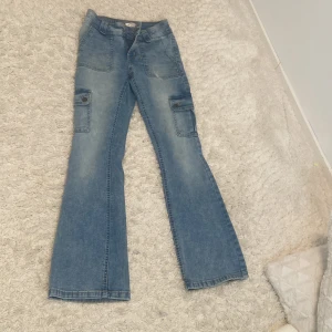 Blå cargojeans med bootcut från Lindex - Snygga ljusblå cargojeans från Lindex i modell Freja, storlek 158. Jeansen har bootcut-ben, stora fickor på sidorna och klassisk jeanslook. Perfekta för dig som gillar en avslappnad och trendig stil. Materialet är mjukt denim i bomull.