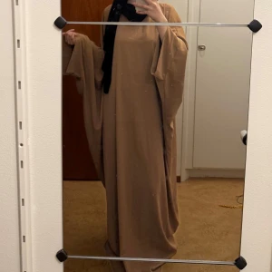 Beige långklänning - Säljer en elegant beige butterfly abaya, vidärmar, stilren, väldigt lös passform perfekt för en mer modest look. Onesize passar XS-L 147cm lång!