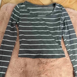 Gråvit randig långärmad tröja - Snygg långärmad tröja i grått med vita horisontella ränder. Modellen är croppad med rund halsringning och sitter tajt mot kroppen. Perfekt till jeans eller kjol för en chill och stilren look. Mjuk och stretchig bomullsblandning. Gammal bild! 