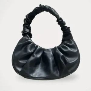 Svart axelväska i skinnimitation - Trendig svart axelväska med scrunchie-inspirerat handtag och rundad form. Väskan är gjord i mjuk skinnimitation och har en magnetknapp som stängning. Perfekt storlek för det viktigaste och ger en cool vibe till din outfit.