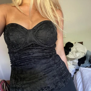 Svart spetsig korsett tubtopp - Svart tubtopp med vadderade kupor och dragkedja i sidan. Framsidan är täckt av spets och baksidan är slät och glansig. Det finns axelband som medföljer om man vill sätta dit dom🪩 köpt second hand🍓