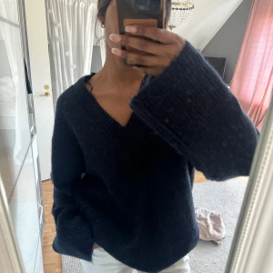 Mörkblå stickad tröja Gina Tricot - Mysig mörkblå stickad tröja från Gina Tricot med v-ringning och extra vida ärmar. Tröjan har en loose passform och är perfekt för kyliga dagar. Materialet är fluffigt och super mjukt. Aldrig använd! 