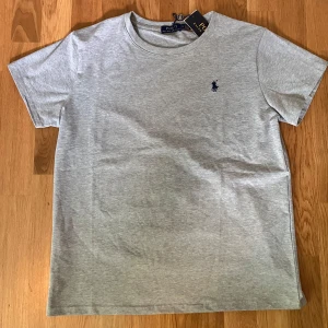 Grå Ralph Lauren t-shirt - Säljer en sprillans ny Ralph Lauren t-shirt som endast burits en gång. Inga defekter alls, 10/10 skick och passformen är perfekt. Ny med prislapp