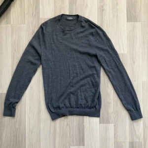 Mörkgrå merinoullströja Dressmann - En stilren mörkgrå tröja från Dressmann i mjuk merinoull. Klassisk rund halsringning och långa ärmar. Perfekt för lager-på-lager och enkel att matcha med jeans eller chinos. Snygg och enkel design som funkar året runt.