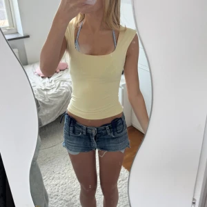 Ljusgul tight linnetopp - Säljer en ljusgul, tight och ärmlös linnetopp med fyrkantig ringning. Toppen är enkel och stilren, perfekt att matcha med jeansshorts eller kjol för en fräsch sommarlook. Materialet känns mjukt och stretchigt för en bekväm passform. Lite sminkfläckar på kanten vid halsen