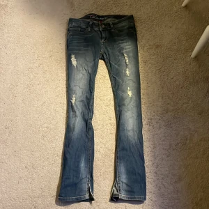 Blå bootcut jeans low waist  - Säljer ett par blå jeans. Jeansen har slitna detaljer framtill, klassiska kontrastsömmar och broderade bakfickor. Materialet är jeans och de har en snygg tvättad look. Jeansen är klippta ner till för att få mer bootcut. Pris diskuteras