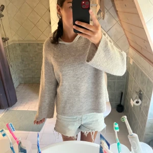 Grå stickad hoodie med vida ärmar - Mysig beige stickad hoodie med vida ärmar och avslappnad passform. Tröjan har huva och är skön o snygg. Enkel o stilren som funkar till många olika outfits