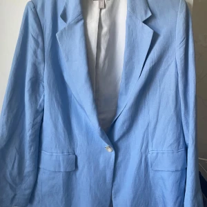 Ljusblå kavaj i linne från H&M - Snygg ljusblå kavaj från H&M i linneblandning med klassisk krage, en knapp framtill och två fickor med lock. Perfekt för en fräsch och stilren look. Lätt och luftig känsla, passar bra till vår och sommar.