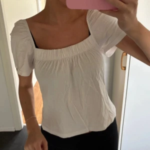 Vit blus med puffärm från H&M - Supersöt vit blus från H&M med puffiga korta ärmar och smockad kant vid halsringningen. Blusen har en luftig passform, perfekt för en fräsch och enkel look.🩷