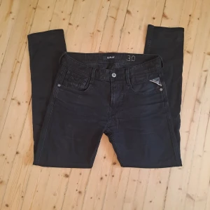 Svarta Replay jeans, storlek 30 - Säljer ett par svarta jeans från Replay i klassisk femficksmodell. Jeansen har raka ben, snygga detaljer på bakfickorna och Replay-logga på läderpatchen bak. Materialet är jeans och färgen är svart, perfekt till en clean och stilren look.