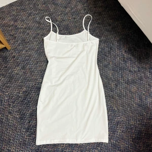 Vit kort klänning - Vit kort klänning med smala axelband från Dennis Maglic. Framtill står det 'baby' i glittriga diamnter.. Klänningen har en tight passform och är gjord i ett mjukt, stretchigt material. 