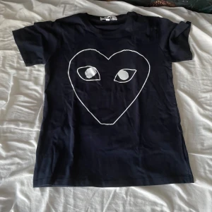 Svart t-shirt Comme des Garçons Play - Svart t-shirt från Comme des Garçons Play med ikoniskt stort hjärta-tryck med ögon på bröstet. Klassisk passform med korta ärmar och rund hals. Tillverkad i mjuk bomull som känns skön mot huden. Perfekt statement-plagg för dig som gillar streetstyle.