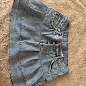 Jeanskjol från Weekday, ljusblå - Säljer en ljusblå jeanskjol från Weekday med klassisk femficksdesign och veckad nederdel. Kjolen är kort och har bälteshällor samt knappar framtill. Perfekt för dig som gillar en avslappnad och trendig stil. SYTT SJÄLV!