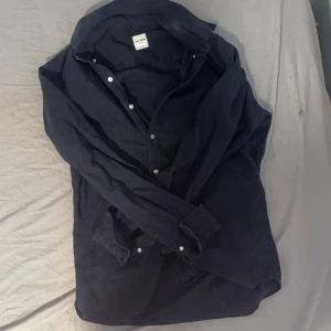 Mörkblå skjorta från John Henric - Snygg mörkblå skjorta från John Henric med klassisk krage och vita knappar. Tillverkad i italienskt tyg av bomull, perfekt för dig som gillar stilrena och tidlösa plagg. Skjortan har lång ärm och passar till många olika looks. Tveka inte på att höra av dig 