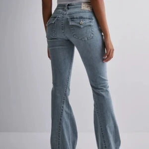 Ljusblå bootcut jeans från True Religion - Säljer ett par ljusblå bootcut jeans från True Religion med ikoniska bakfickor och snygga detaljer. Jeansen har klassisk femficksdesign, normal passform och är tillverkade i mjukt denim. Perfekta för dig som gillar en avslappnad men trendig look.