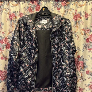 Burberry vindjacka med logomönster  - Snygg svart vindjacka från Burberry med heltryckt logomönster i vitt, grått och rött. Jackan har huva, dragkedja framtill och är tillverkad i glansig polyester. Perfekt för dig som vill sticka ut med en exklusiv streetstyle-look.