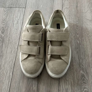 Beige sneakers i mocka med kardborre - Snygga beige sneakers från Sneaky Steve i mjuk mocka med två breda kardborreband. De är endast använda en gång då de inte passade. Original pris är 1800, där av är mitt pris väldigt bra då jag bara vill få de sålda just nu❤️❤️