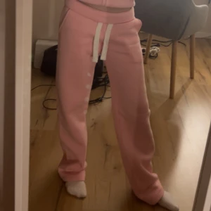Rosa mjukisbyxor med snörning RUSSEMERCH  - Säljer ett par ljusrosa mjukisbyxor med vit snörning i midjan. Byxorna har en avslappnad passform och är perfekta för chill dagar. Tillverkade i mjukt material som känns skönt mot huden.