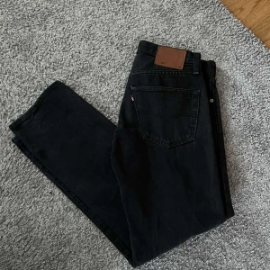 Svarta Levi's 501 jeans 31/30 - Säljer ett par klassiska svarta Levi's 501 jeans i rak modell. Jeansen har fem fickor, knappgylf och den ikoniska läderpatchen bak i midjan. Perfekta för dig som gillar tidlös stil och vill ha ett par jeans som funkar till allt.