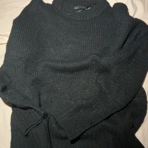 Svart stickad tröja från 157 XS/S - Mysig svart stickad tröja från 157 i storlek XS/S. Tröjan har en högre ribbad hals och långa ärmar, perfekt för kyliga dagar. Enkel och stilren design som funkar till många outfits. Snygg att bära både till jeans och kjol.