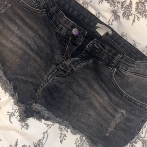 Svarta jeansshorts med fransig kant - Snygga svarta jeansshorts med slitna detaljer och fransig kant nertill. Klassisk femficksmodell med dragkedja och knapp. Perfekta för en chill sommarlook och passar till allt. Mörk tvätt och coolt sliten finish.
