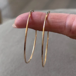 Stora guldiga hoops örhängen - Säljer ett par stora, tunna hoops i guldig metall. De är klassiskt runda och ger en snygg statement-look till vilken outfit som helst. Perfekta för dig som gillar enkel men trendig stil.