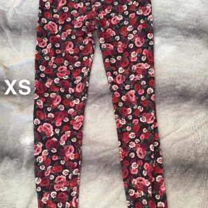 Blommiga leggings XS - Supersnygga leggings i XS med blommigt mönster i rött, rosa och vitt på svart botten. Tight passform och stretchigt material som sitter skönt hela dagen. Perfekta för dig som vill sticka ut med färg och mönster! 🌸Fint använt skick. Storlekslapp borta men uppskattningsvis XS