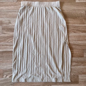 Beige sommarkjol - Säljer en beige ribbad långkjol från NLY Trend i storlek XS. Kjolen har en rak passform, elastisk midja och diskret slits på sidan. Perfekt för dig som gillar en clean och stilren look med mjukt material och snygga vertikala ränder.
