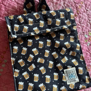 Svart lunch bag med ölglas-mönster - Unik svart lunch bag från See My Bag med ölglas-mönster över hela väskan. Väskan är handgjord och har ett isolerat, silvrigt innerfoder som håller innehållet kallt. Perfekt för picknick eller häng i parken. Stängs med kardborreband och har praktiska axelremmar.