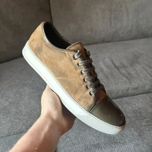 SÖKER BYTE - Snygga sneakers i beige mocka med grå snörning och tåparti i mörkgrått skinn. Skorna har vit platt sula och rund tå, vilket ger en clean och stilren look. Perfekta för dig som gillar en avslappnad men ändå trendig stil.